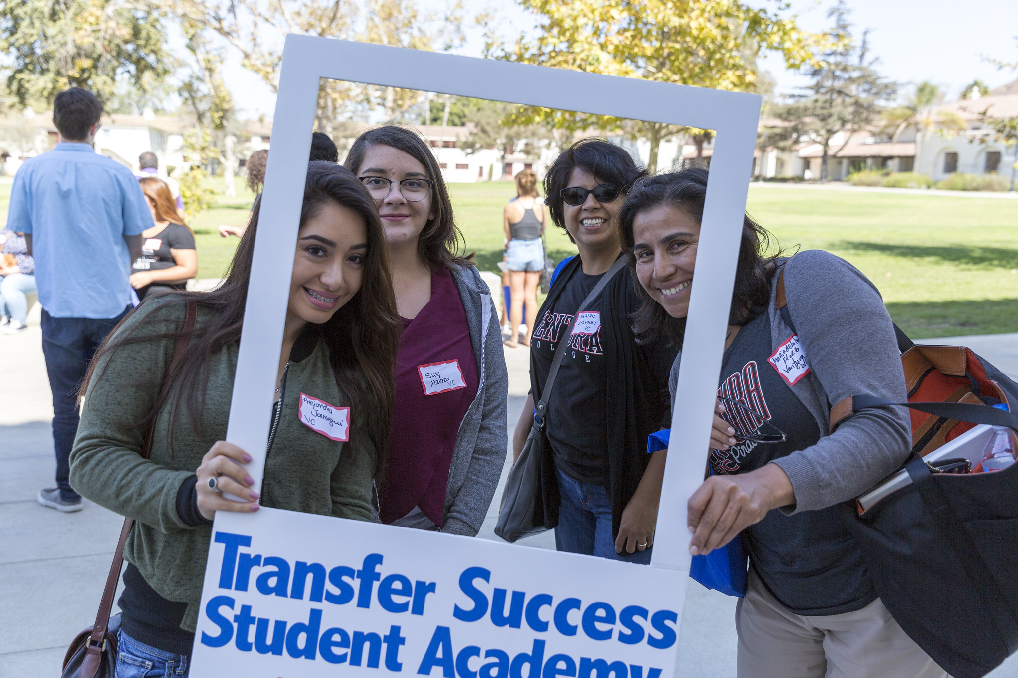 Two young women and their mothers hold a sign that reads Transfer Student Success Academy.