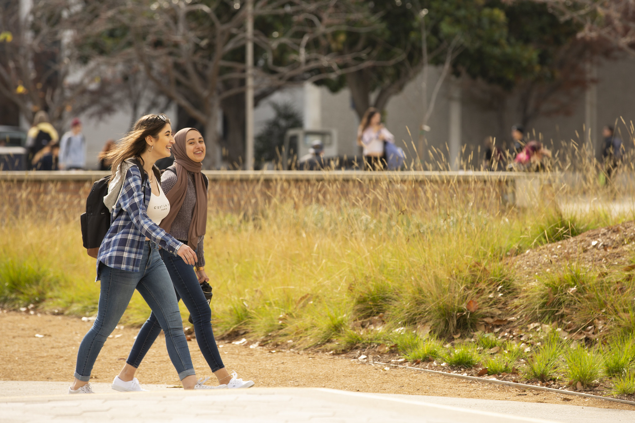 Two young women walking across a college campus talking with one another.