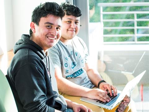 Two smiling college students balancing laptops on their laps.