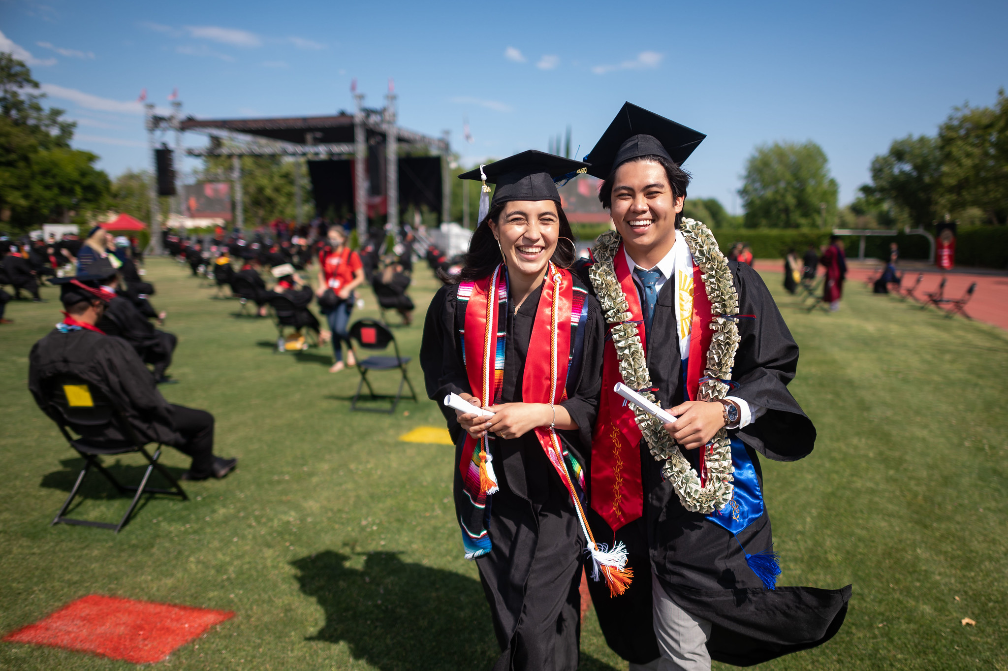 Two graduates walking across a grassy field.