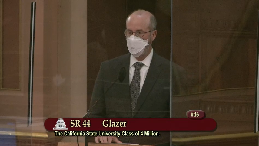 man wearing protective face mask standing at podium behind glass at California State Senate