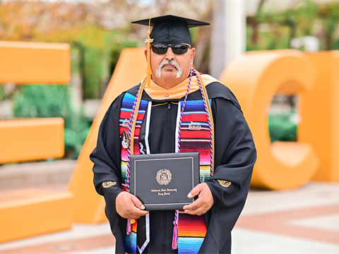 Joseph Valadez posing with sunglasses on in his CSULB graduation cap and gown.