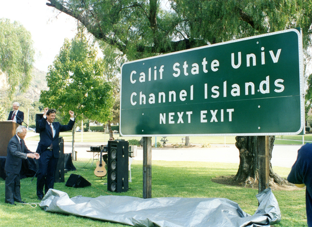 CHANNEL ISLANDS   1999 California State Assembly members Nao Takasugi (left) and Jack O’Connell (right) reveal the official campus road sign to be placed along the 101 Freeway in Camarillo during the planning stages of the university. The campus officially opens three years later.