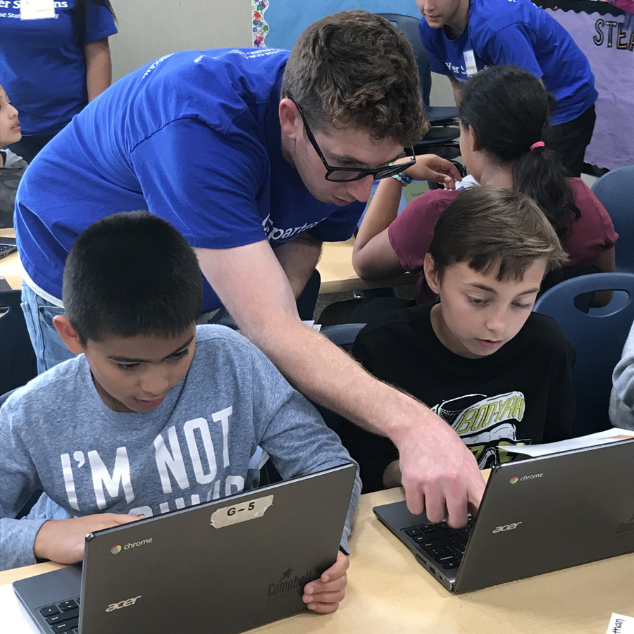 SJSU student Christopher Conetta helping two boys on laptops through the Cyber Spartans program.