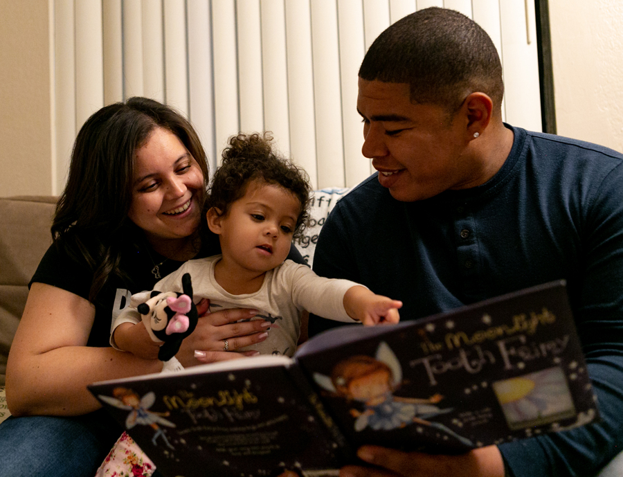 Steven reading a children’s book with his wife and daughter.