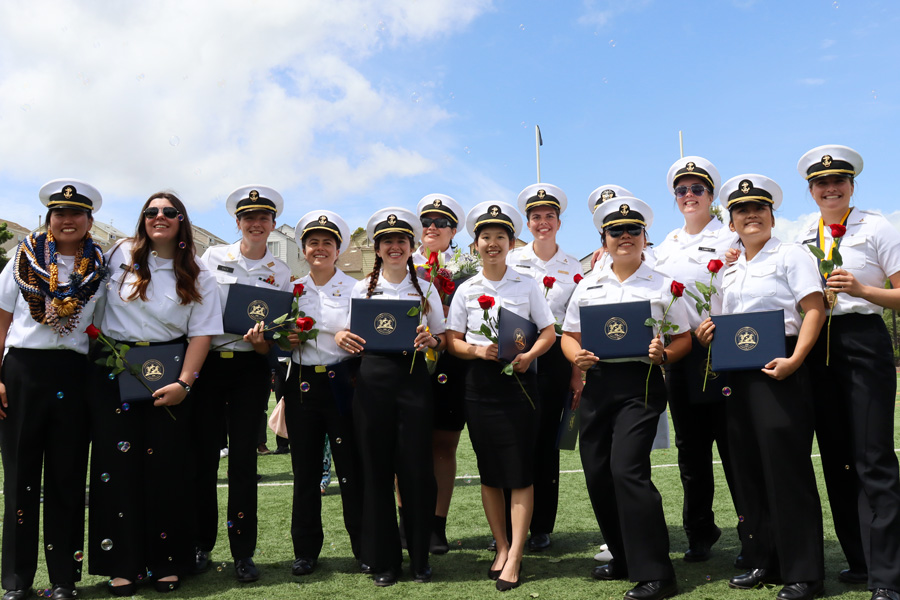graduating female cadets smile and hold up diplomas