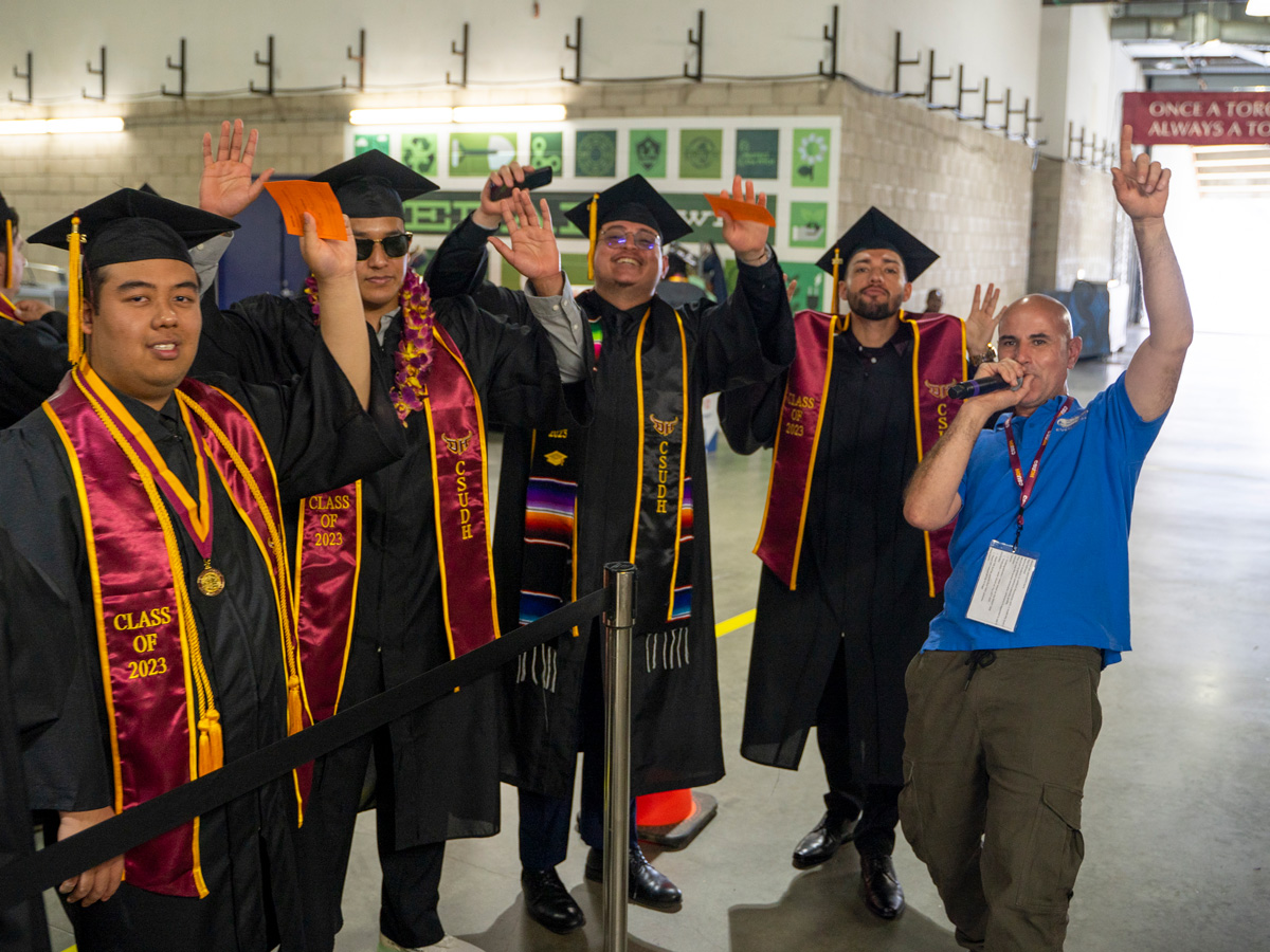 graduates and a man with a microphone raising their arms in celebration